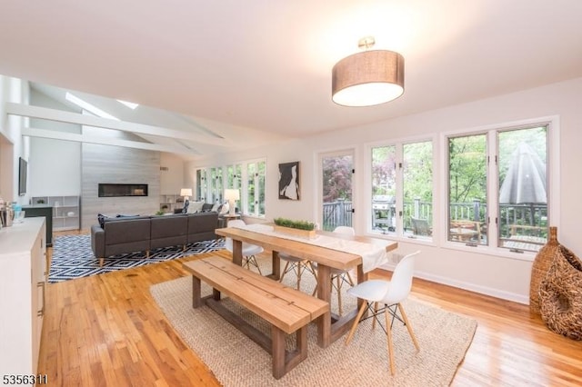 dining area featuring healthy amount of natural light, light wood-style flooring, a large fireplace, and baseboards