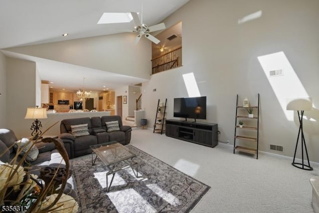 living area with a ceiling fan, a skylight, light colored carpet, high vaulted ceiling, and stairway