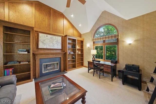carpeted office space with a ceiling fan, a fireplace with flush hearth, high vaulted ceiling, and built in shelves