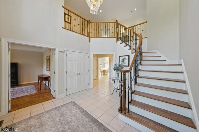 stairs with tile patterned floors, a towering ceiling, a chandelier, and baseboards