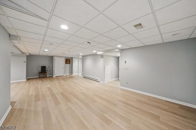 finished below grade area featuring a baseboard heating unit, light wood-type flooring, baseboards, recessed lighting, and a drop ceiling