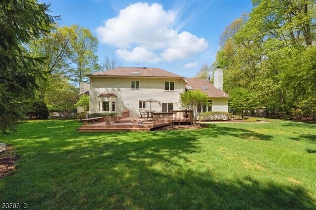 back of property with a wooden deck, a chimney, and a yard