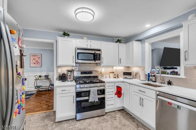 kitchen featuring appliances with stainless steel finishes, a sink, light countertops, white cabinets, and ornamental molding
