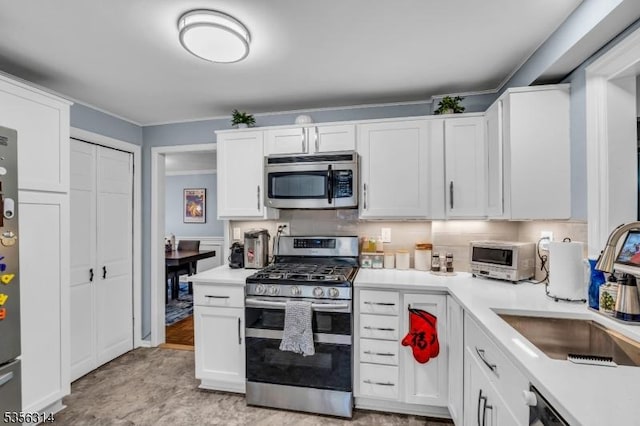 kitchen featuring appliances with stainless steel finishes, a sink, light countertops, white cabinets, and crown molding