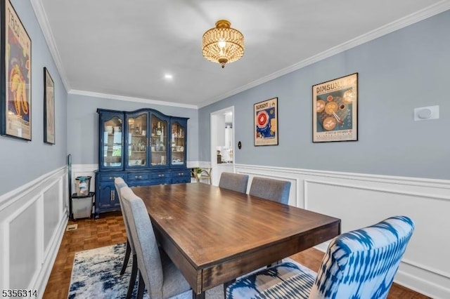 dining area with crown molding, a wainscoted wall, and a decorative wall