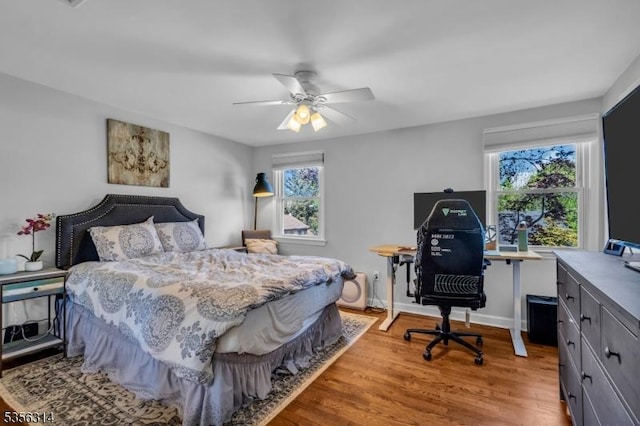 bedroom featuring multiple windows, wood finished floors, an office area, and a ceiling fan