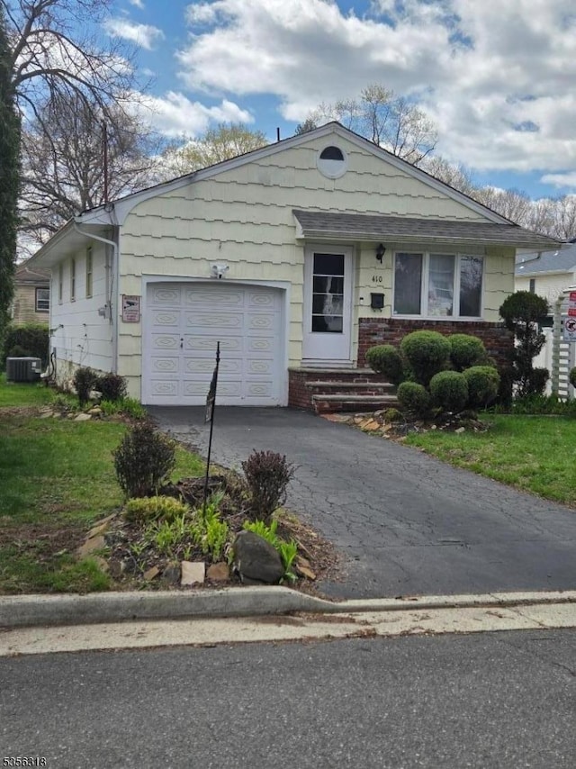 view of front of home featuring asphalt driveway, an attached garage, central AC unit, and a front yard