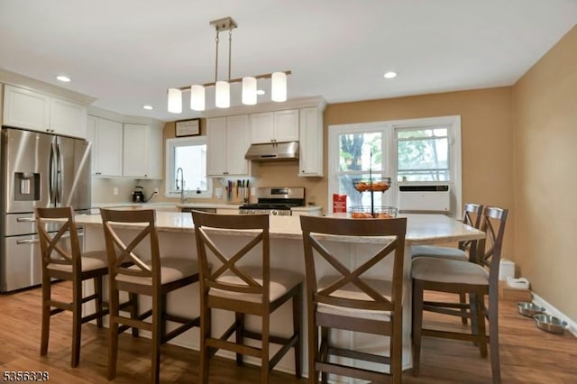 kitchen with appliances with stainless steel finishes, under cabinet range hood, light countertops, plenty of natural light, and recessed lighting