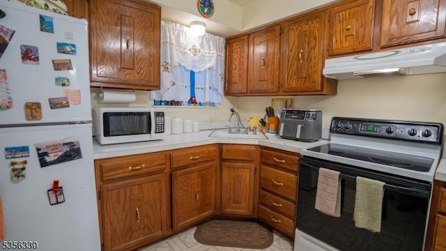 kitchen featuring white appliances, under cabinet range hood, a sink, and brown cabinets