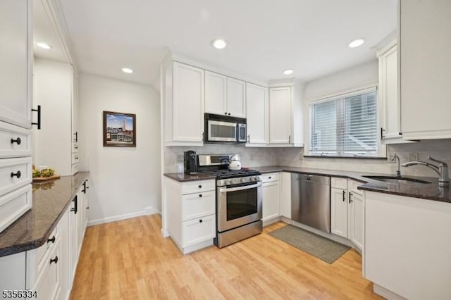 kitchen with appliances with stainless steel finishes, a sink, light wood-type flooring, white cabinets, and recessed lighting