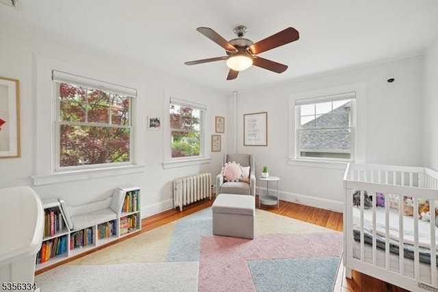 bedroom with radiator heating unit, a crib, wood finished floors, and baseboards