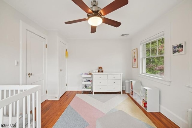 bedroom with light wood-type flooring, baseboards, ceiling fan, and a nursery area