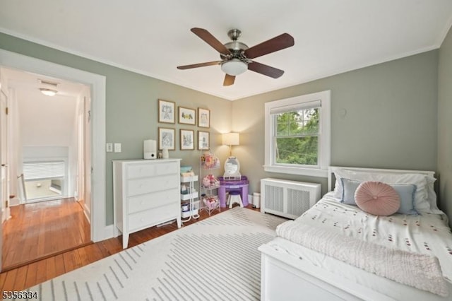bedroom with radiator heating unit, wood finished floors, crown molding, baseboards, and a ceiling fan