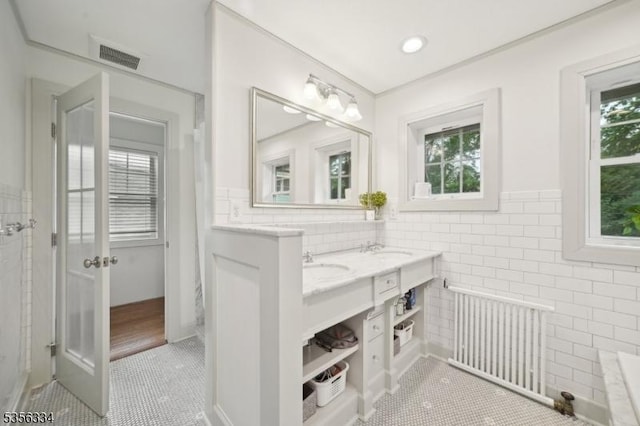 bathroom featuring radiator heating unit, tile patterned floors, tile walls, wainscoting, and double vanity