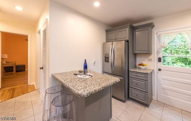kitchen with stainless steel fridge, gray cabinets, light tile patterned floors, recessed lighting, and light stone counters