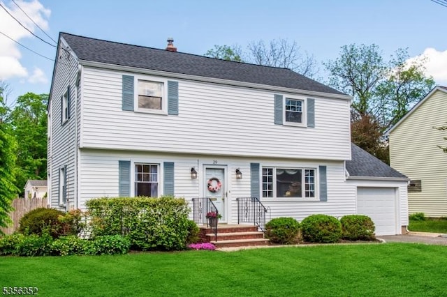 colonial-style house featuring a chimney, asphalt driveway, a garage, and a shingled roof