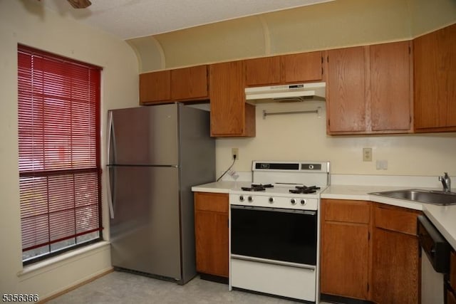 kitchen with appliances with stainless steel finishes, under cabinet range hood, a sink, light countertops, and brown cabinetry