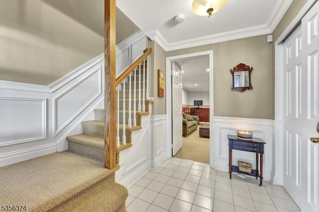 stairway with a decorative wall, tile patterned flooring, crown molding, a wainscoted wall, and carpet floors