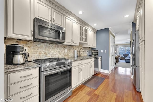 kitchen with appliances with stainless steel finishes, a sink, light wood-style floors, tasteful backsplash, and baseboards