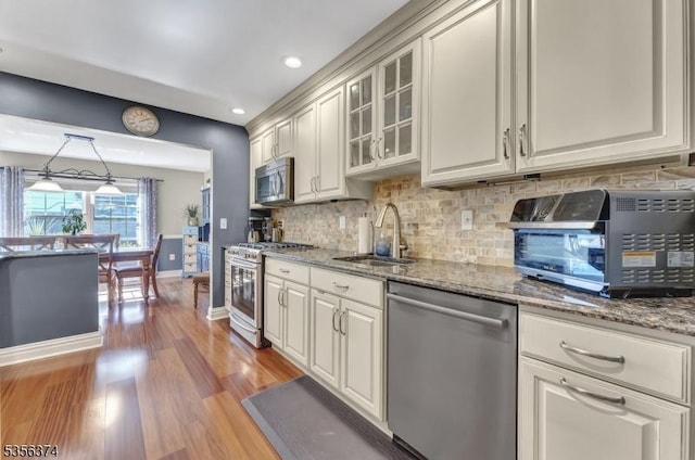 kitchen featuring stainless steel appliances, a sink, baseboards, decorative backsplash, and light wood-type flooring