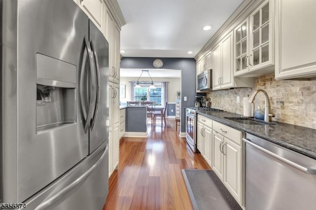 kitchen with appliances with stainless steel finishes, a sink, recessed lighting, glass insert cabinets, and tasteful backsplash