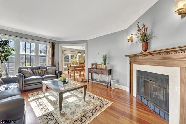 living area with crown molding, light wood-type flooring, and a glass covered fireplace