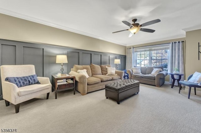 living area featuring a decorative wall, light colored carpet, crown molding, and a ceiling fan