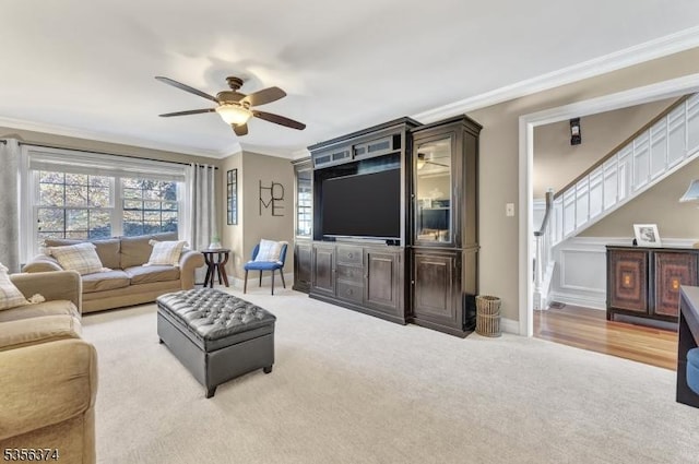 living room featuring ornamental molding, ceiling fan, carpet, stairs, and baseboards