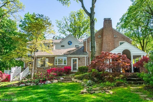 rear view of property with a chimney, a lawn, and stairs