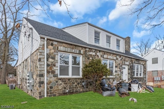 797 Passaic Ave, West Caldwell Twp, NJ 07006 - rear view of house featuring stone siding, a yard, a chimney, roof with shingles, and central AC unit