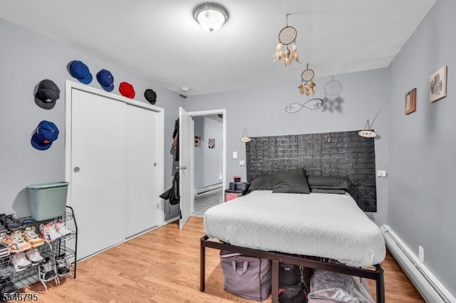 bedroom featuring a baseboard radiator, light wood-style floors, a closet, and a chandelier