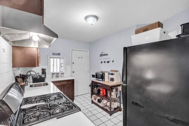 kitchen with freestanding refrigerator, a sink, light countertops, ventilation hood, and light tile patterned flooring