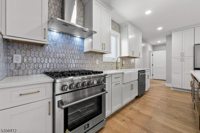 kitchen featuring wall chimney exhaust hood, appliances with stainless steel finishes, light countertops, white cabinets, and recessed lighting