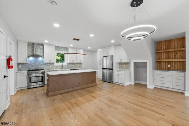 kitchen with stainless steel appliances, wall chimney range hood, tasteful backsplash, light countertops, and white cabinets