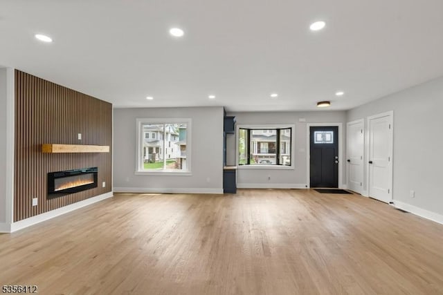 unfurnished living room with light wood-type flooring, recessed lighting, baseboards, and a glass covered fireplace
