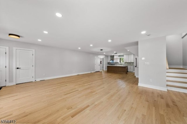unfurnished living room with baseboards, recessed lighting, light wood-type flooring, and stairway