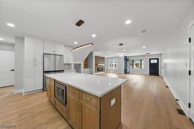 kitchen with appliances with stainless steel finishes, white cabinets, a kitchen island, light wood-style floors, and recessed lighting