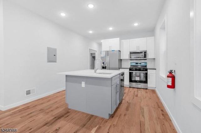 kitchen featuring appliances with stainless steel finishes, a sink, light wood-type flooring, baseboards, and an island with sink
