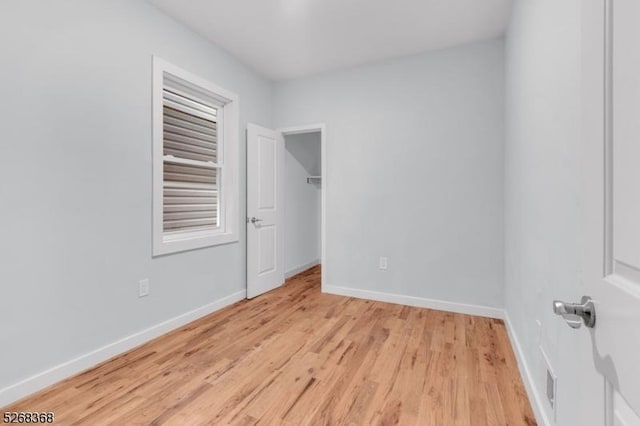 unfurnished bedroom with light wood-type flooring, baseboards, and a spacious closet
