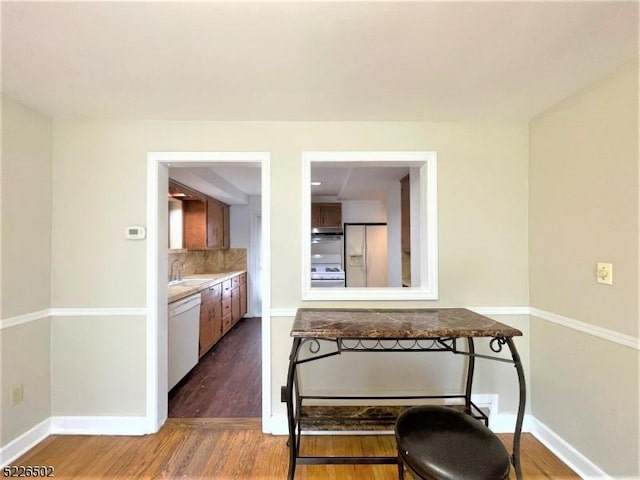 kitchen with white appliances, a sink, wood finished floors, backsplash, and light countertops