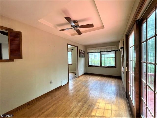 empty room featuring wood finished floors, ceiling fan, baseboards, and a raised ceiling