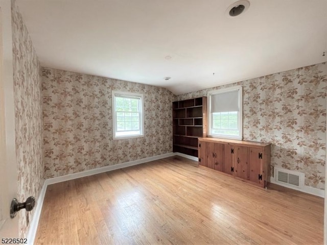 spare room featuring light wood-style floors, wallpapered walls, and baseboards