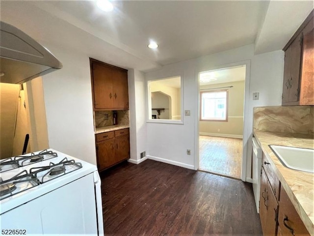 kitchen featuring white gas stove, light countertops, dark wood-type flooring, a sink, and baseboards