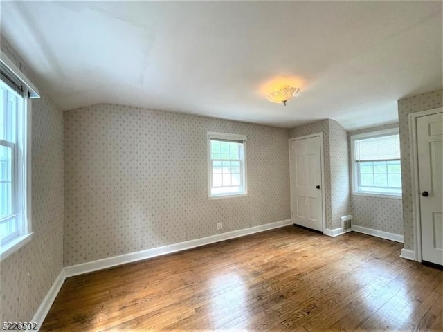 additional living space featuring wallpapered walls, wood finished floors, healthy amount of natural light, lofted ceiling, and baseboards