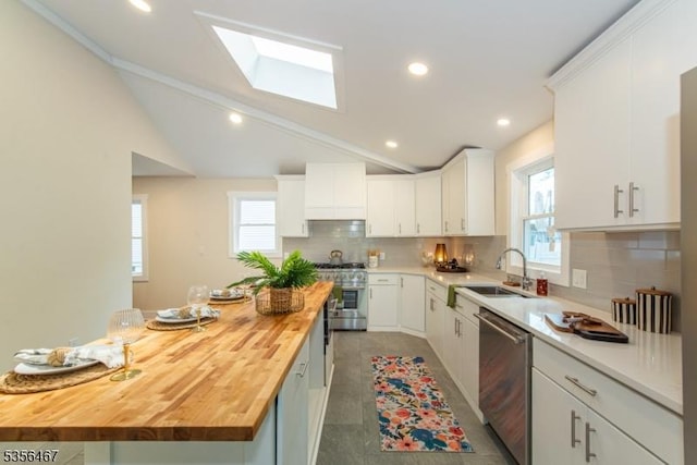 kitchen featuring wood counters, stainless steel appliances, a sink, a skylight, and tasteful backsplash