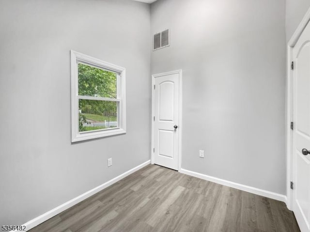 unfurnished bedroom with wood finished floors, baseboards, and a towering ceiling