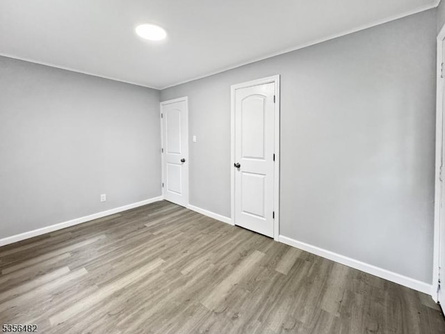 empty room featuring wood finished floors, baseboards, and ornamental molding