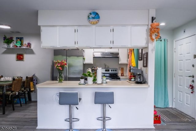 kitchen with stainless steel appliances, under cabinet range hood, wood finished floors, white cabinetry, and a peninsula