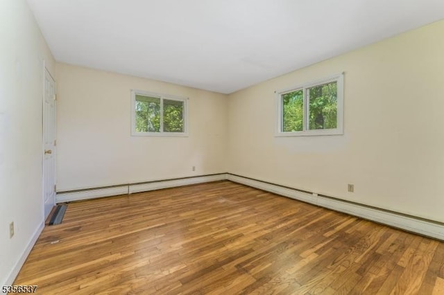 empty room featuring wood finished floors, baseboard heating, and baseboards
