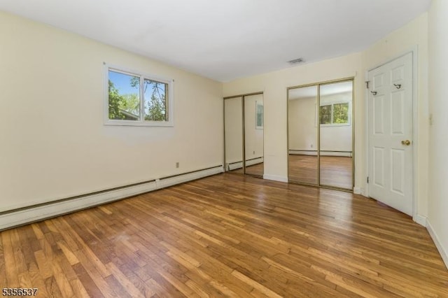 unfurnished bedroom featuring multiple closets, multiple windows, wood finished floors, and baseboard heating